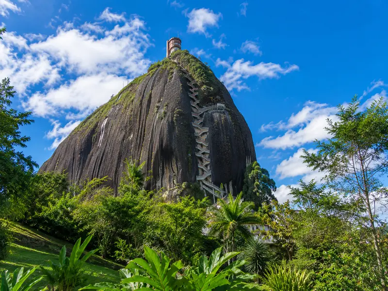 La Piedra del Peñol monolith with its zigzag staircase rising above green foliage in Guatapé, Colombia